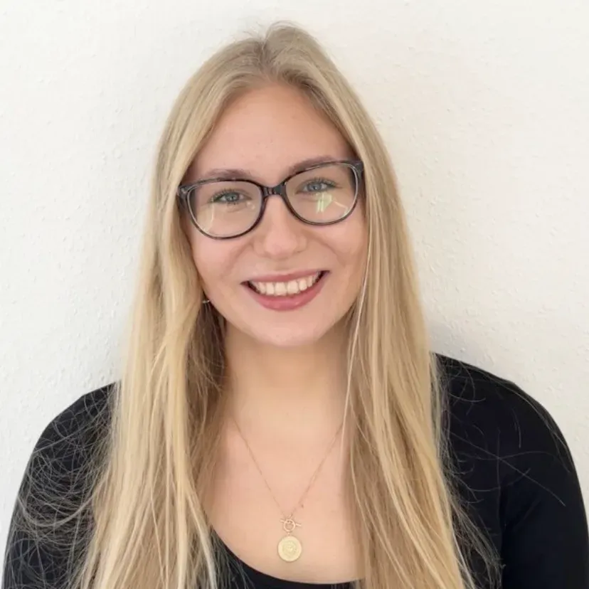 Ein Profilbild von Mareike Jander. Sie trägt einen schwarzen Pullover und steht vor einer weißen Wand. Sie hat lange blonde Haare und trägt eine schwarze Brille.