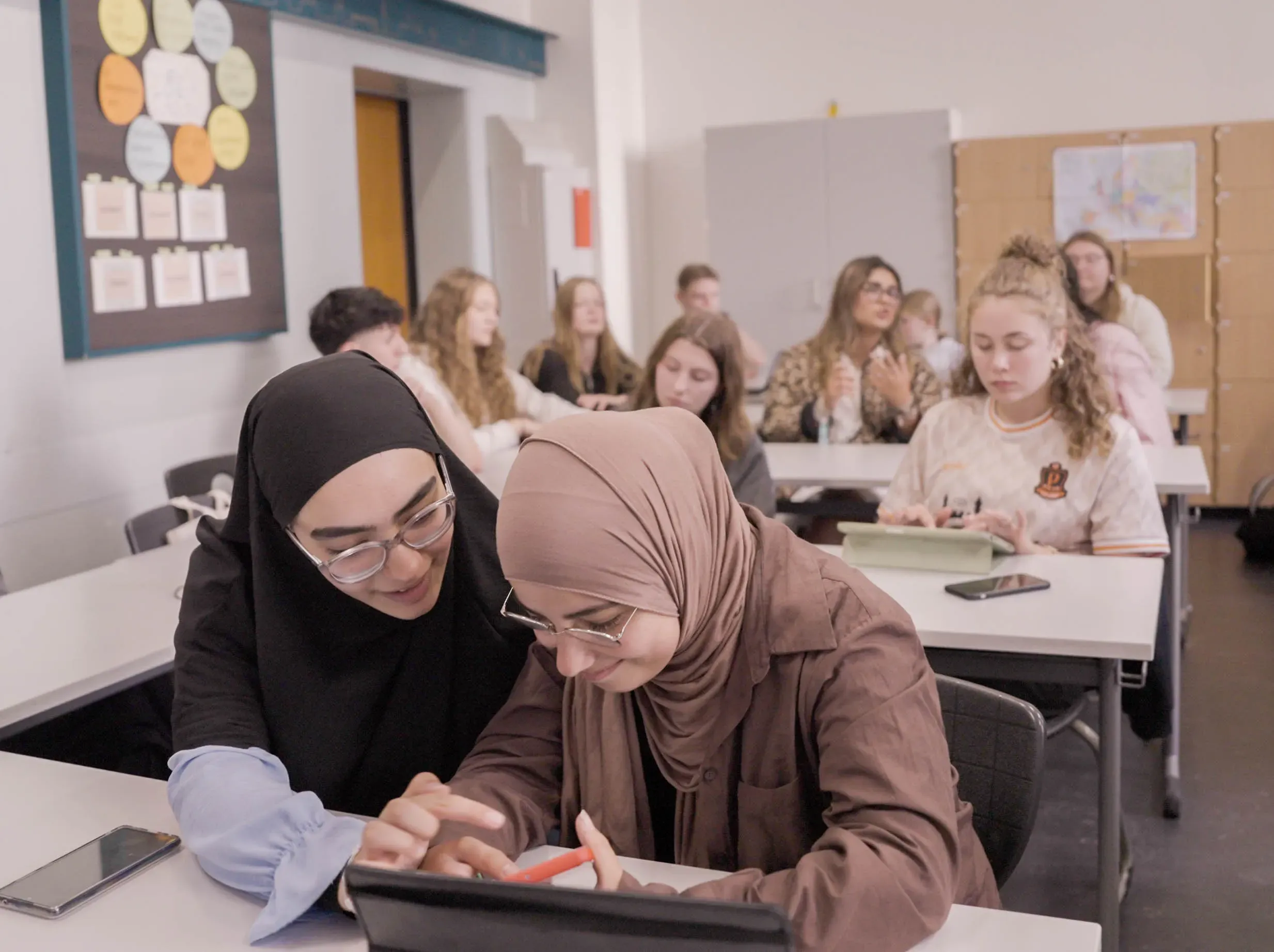 Schüler:innen sitzen im Klassenzimmer und arbeiten mit ihren digitalen Geräten