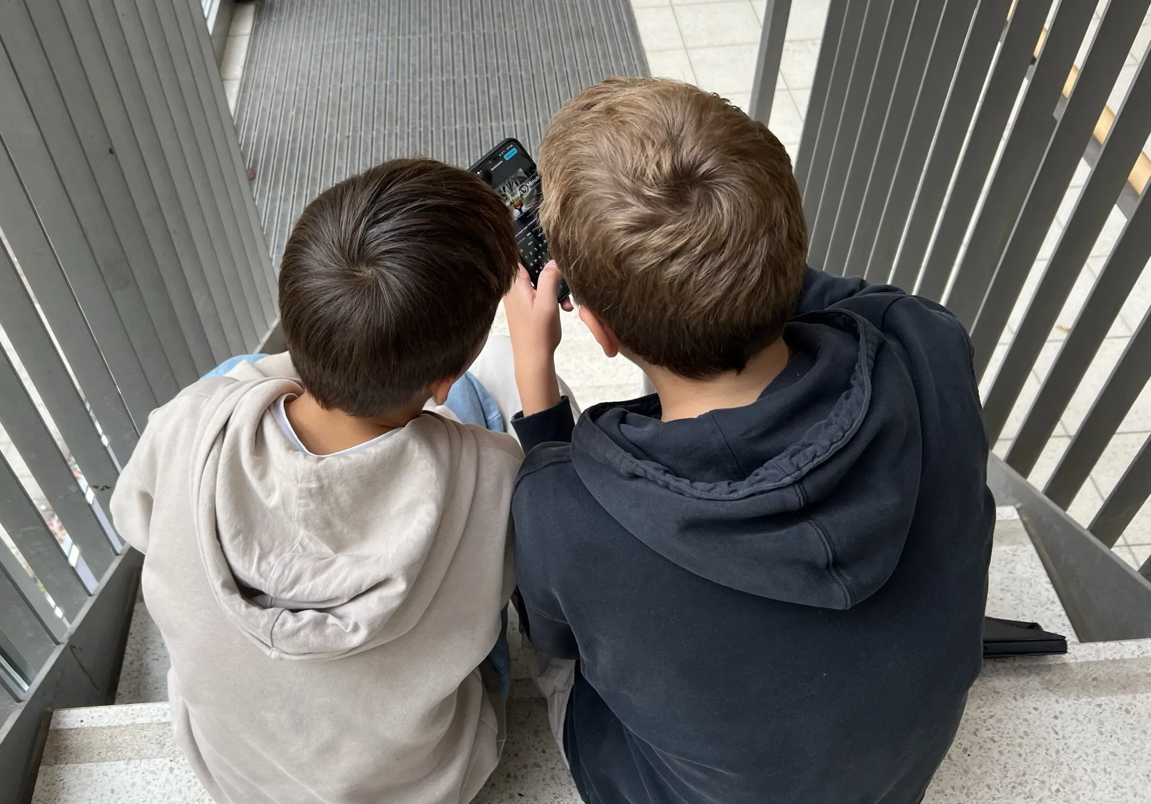 Zwei Jungen sitzen auf einer Treppe und schauen auf ein Smartphone