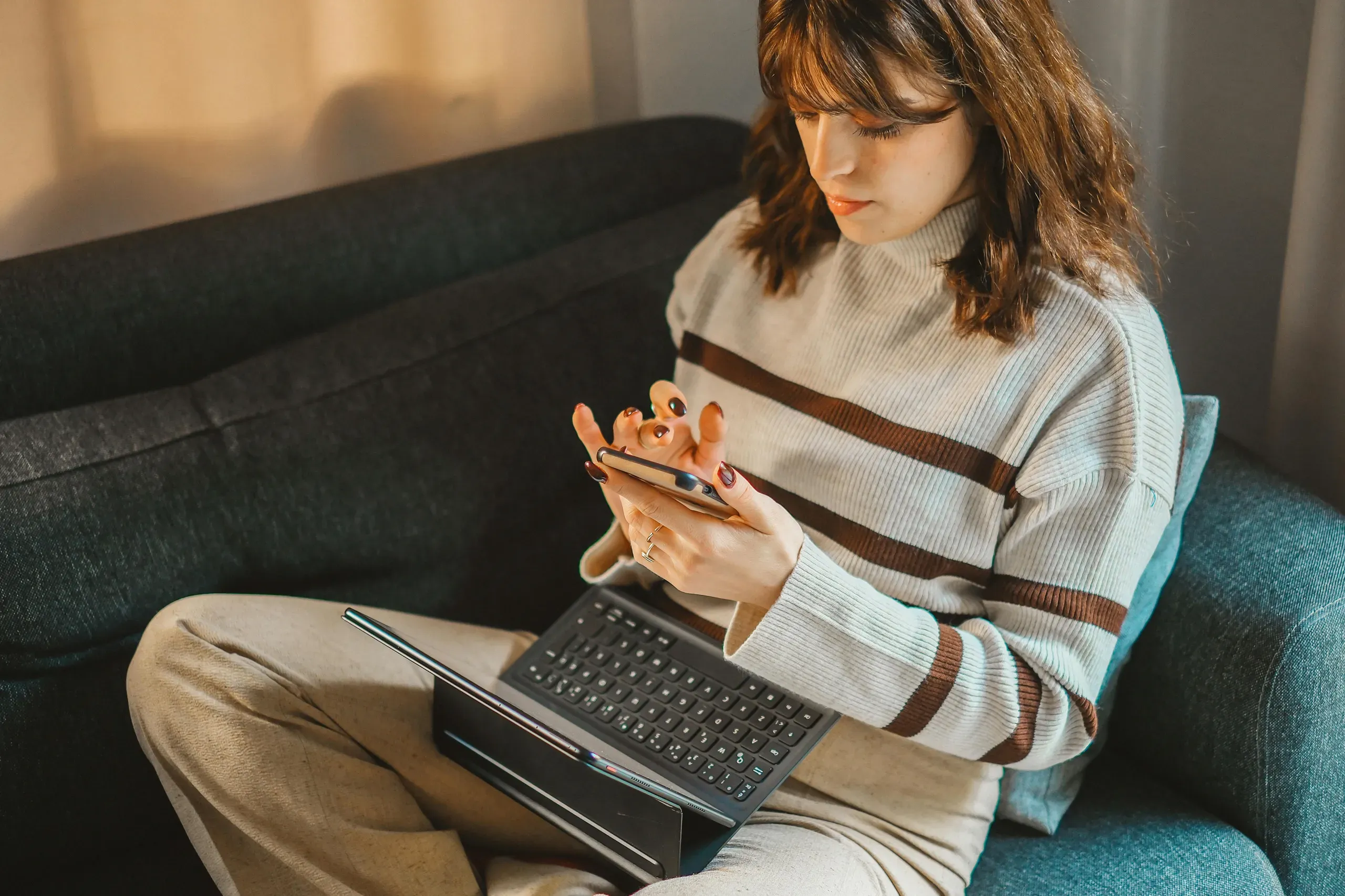 Eine Jugendliche sitzt auf dem Sofa, ein Smartphone in der Hand und ein Tablet auf dem Schoß.